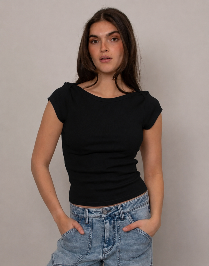 A woman modeling a black short-sleeve top with a wide boat neckline and light-wash blue jeans, standing against a plain light gray studio background.