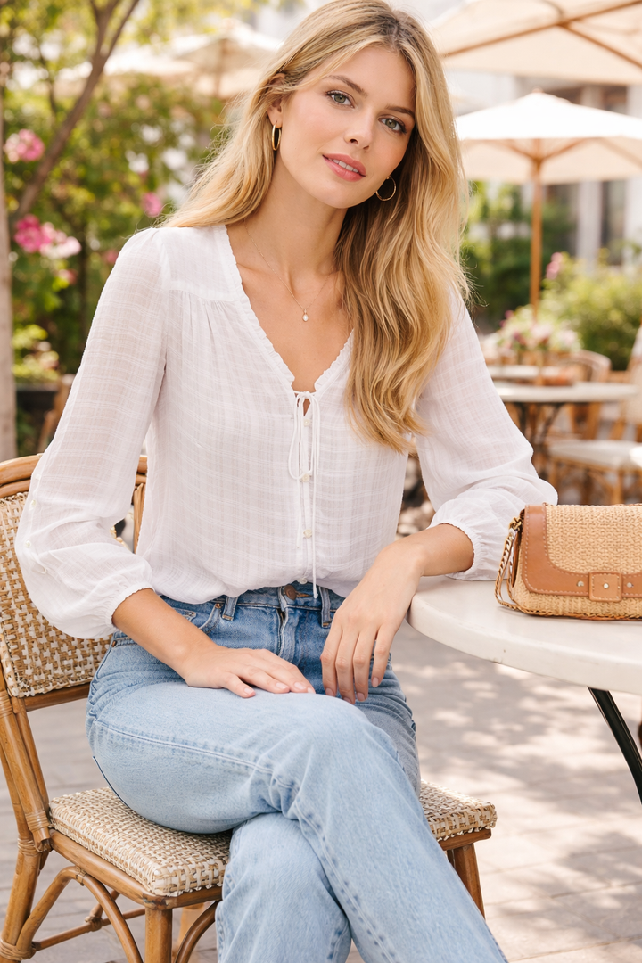 Woman sitting outdoors wearing a white blouse and blue jeans, holding a brown handbag.