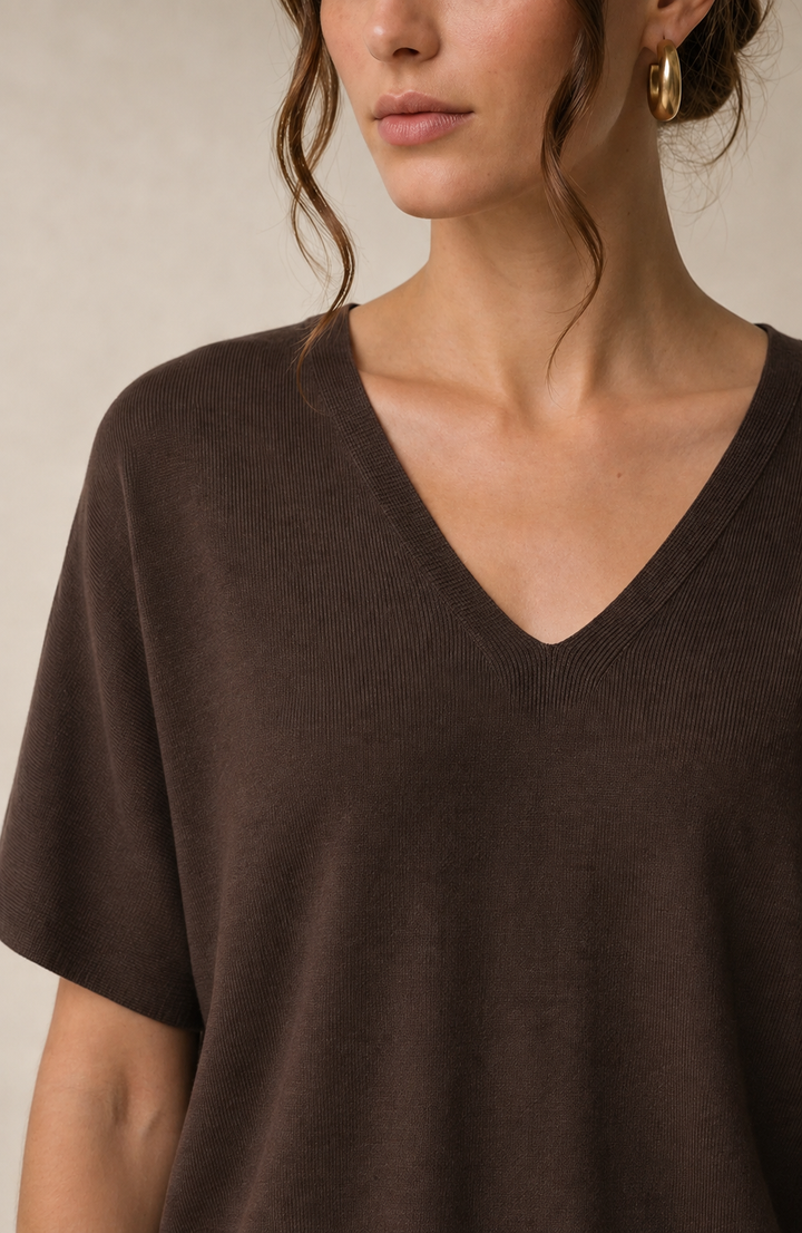 A close-up of a woman wearing a dark brown short-sleeve V-neck knit top against a neutral beige background.