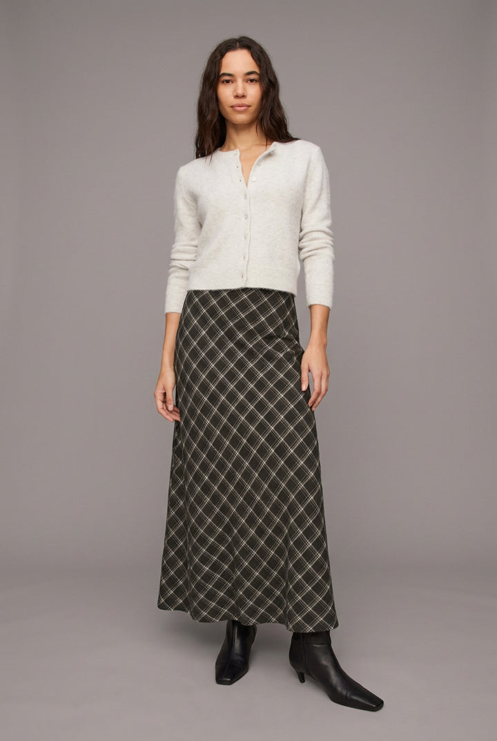 A woman modeling a light gray knit cardigan and a black-and-white diamond-patterned maxi skirt, paired with black pointed-toe ankle boots, against a solid light beige studio background.